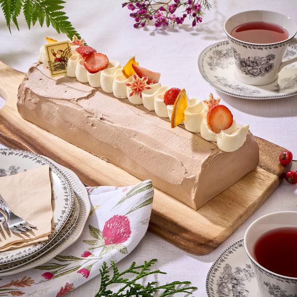 Christmas log cake in pale earl grey icing with cream swirls, strawberries and orange