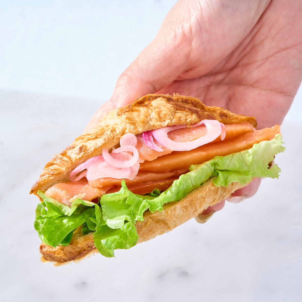 Croissant sandwich with smoked salmon, lettuce and pickled red onion
