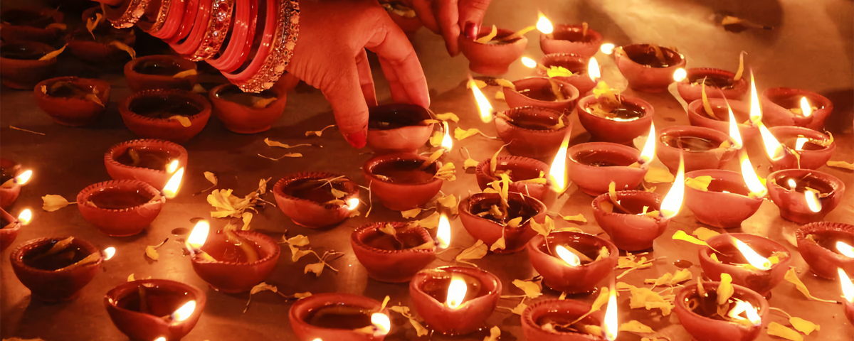 Hands lighting rows of clay diyas scattered with marigold petals, celebrating Deepavali, the festival of lights
