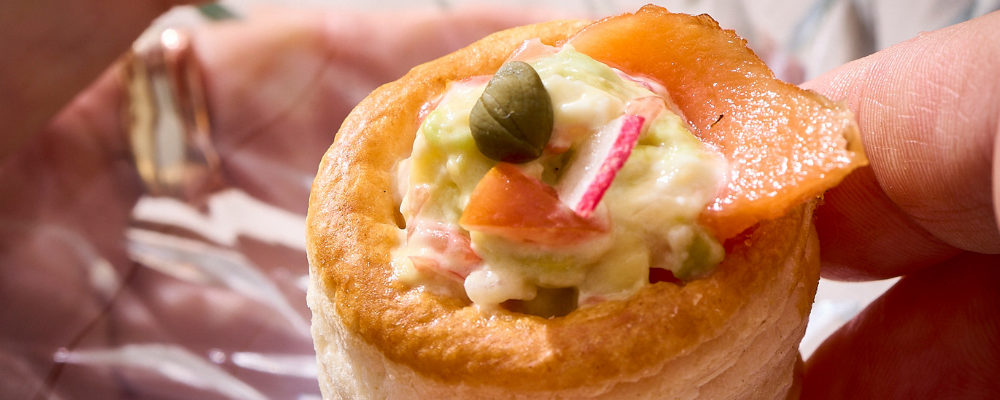Hand holding a smoked salmon vol-au-vent canapé topped with a caper