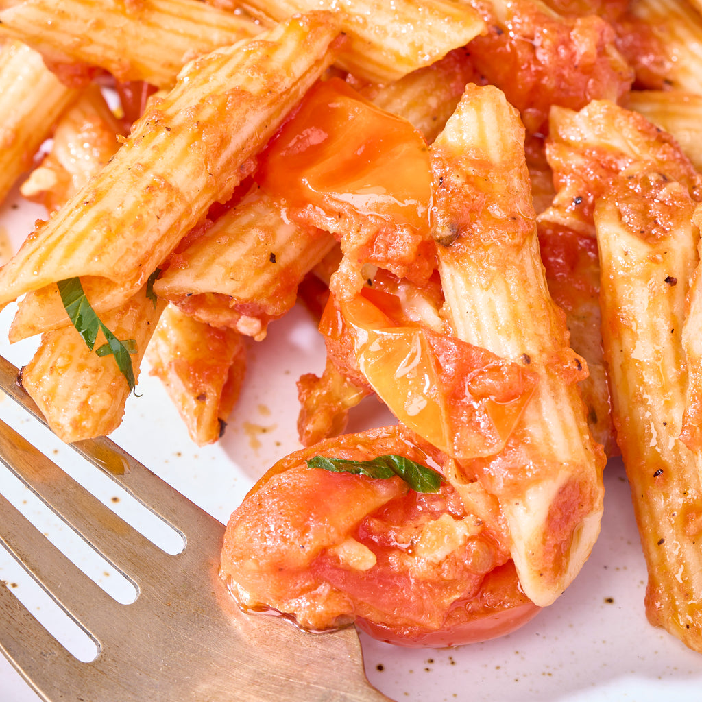 Fork beside penne in cherry tomato sauce with a basil leaf, served from the fennel sausage pasta tray