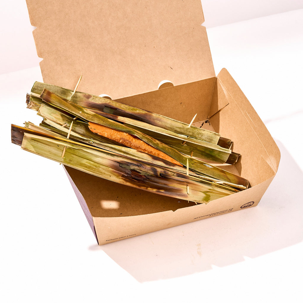 Optional otak otak add-on: grilled fish paste parcels wrapped in leaves inside an open kraft box