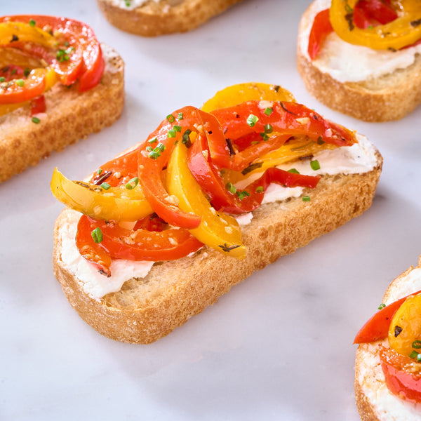 Close-up of Marinated Peppers & Feta on Crostini topped with roasted red and yellow peppers and chives