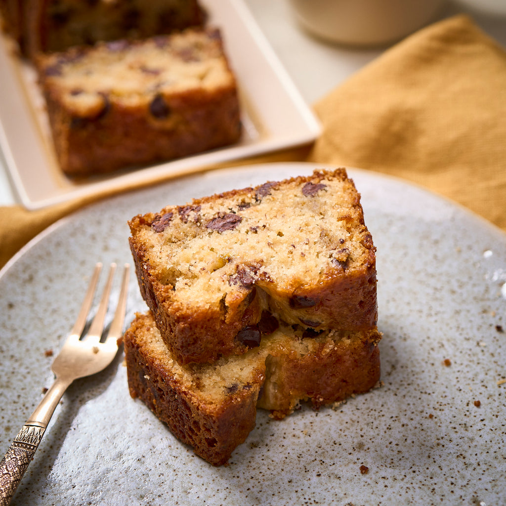 Two slices of banana chocolate chip loaf stacked on a speckled plate with a fork, showing the soft, moist crumb
