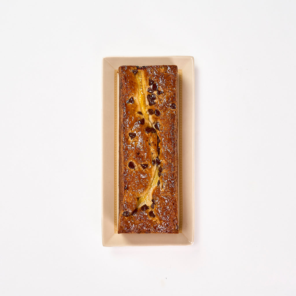 Whole Banana Chocolate Chip Voyage Cake from above, topped with a split banana and chocolate chips on a cream platter