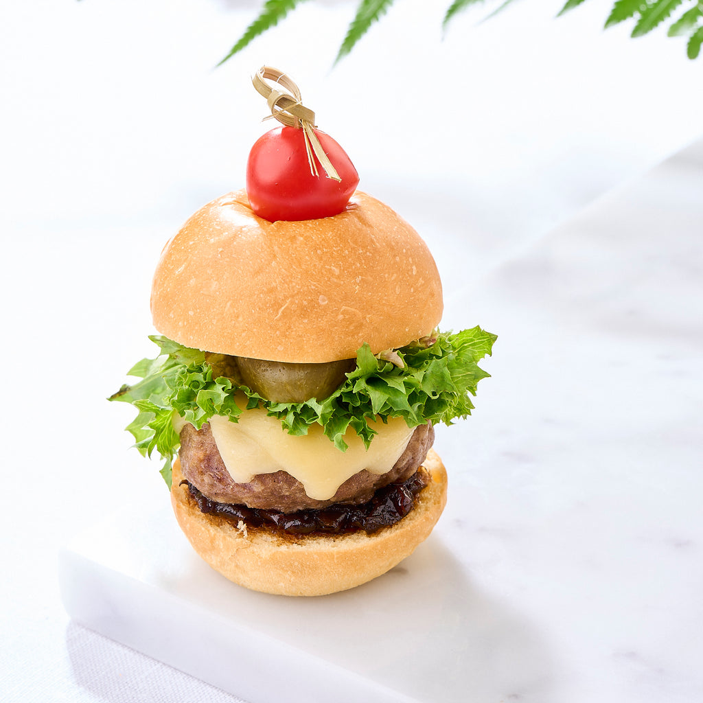 One slider standing tall with melted cheese, frilly lettuce and a cherry tomato pick