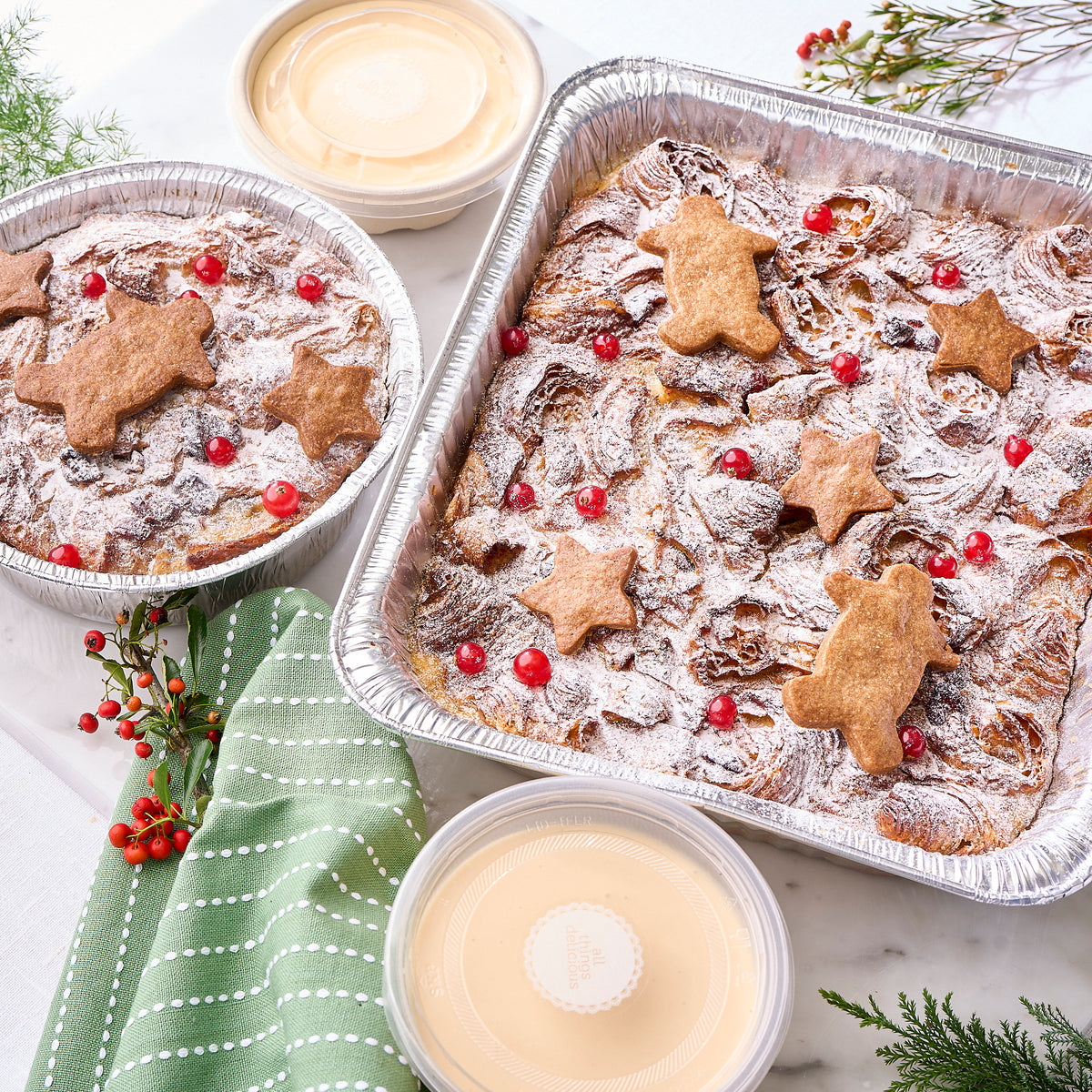 Trays of bread and butter pudding dusted with sugar, beside tubs of crème anglaise