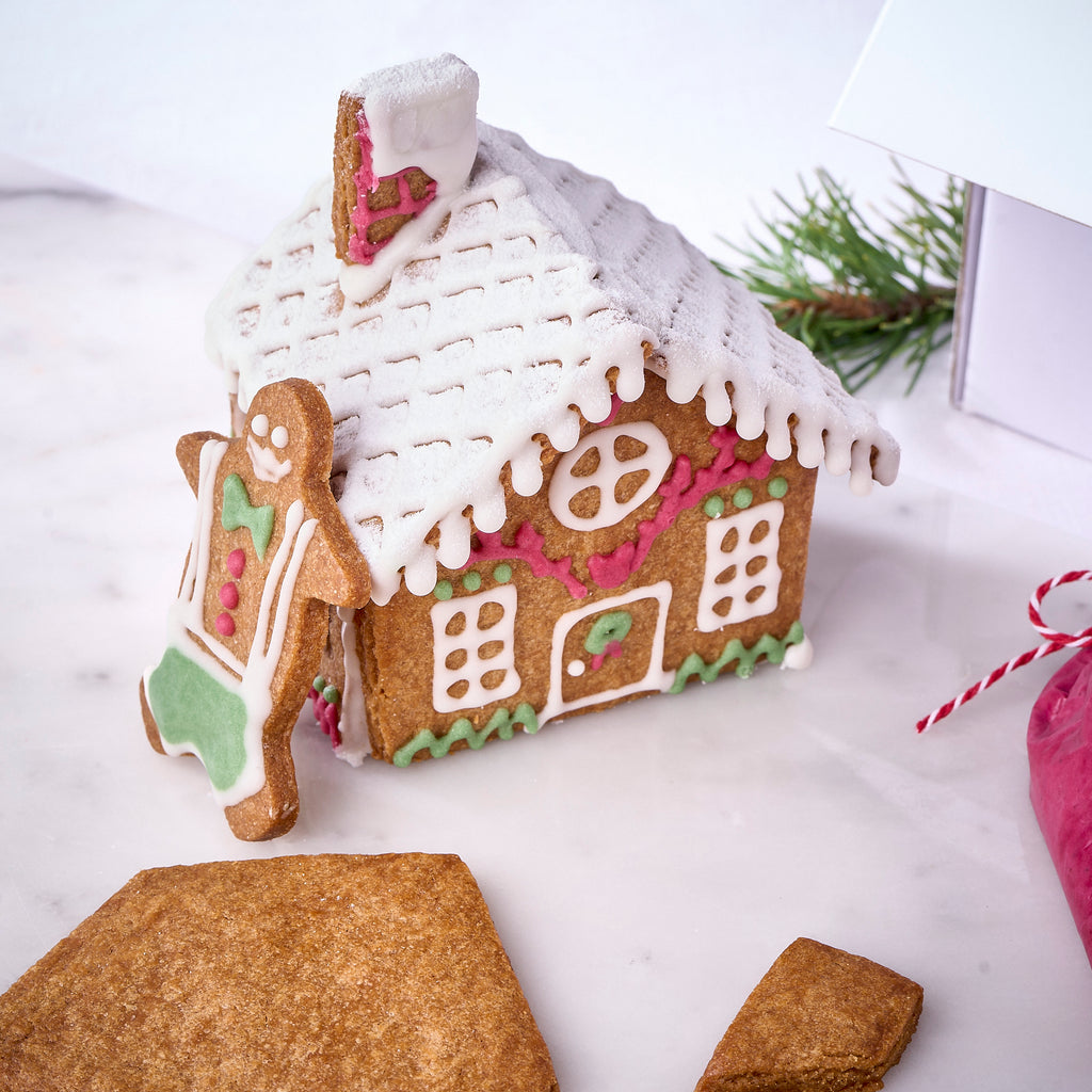 A built gingerbread house iced in white, pink and green, with a gingerbread man