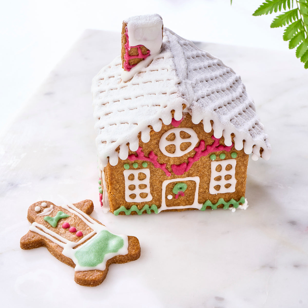 A finished Christmas gingerbread house with an iced gingerbread man on marble