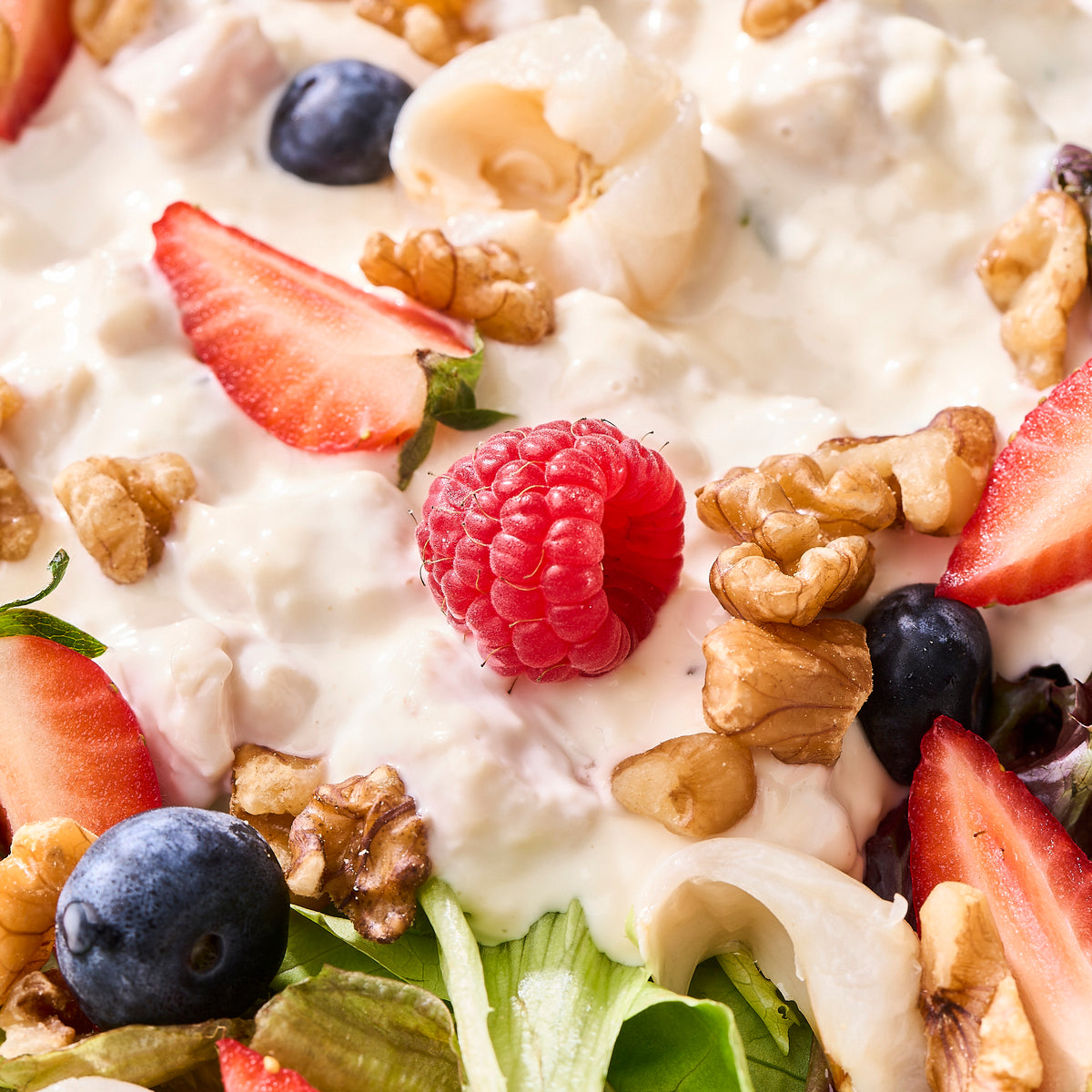 Close-up of strawberries, blueberries, raspberry and walnuts over creamy turkey salad