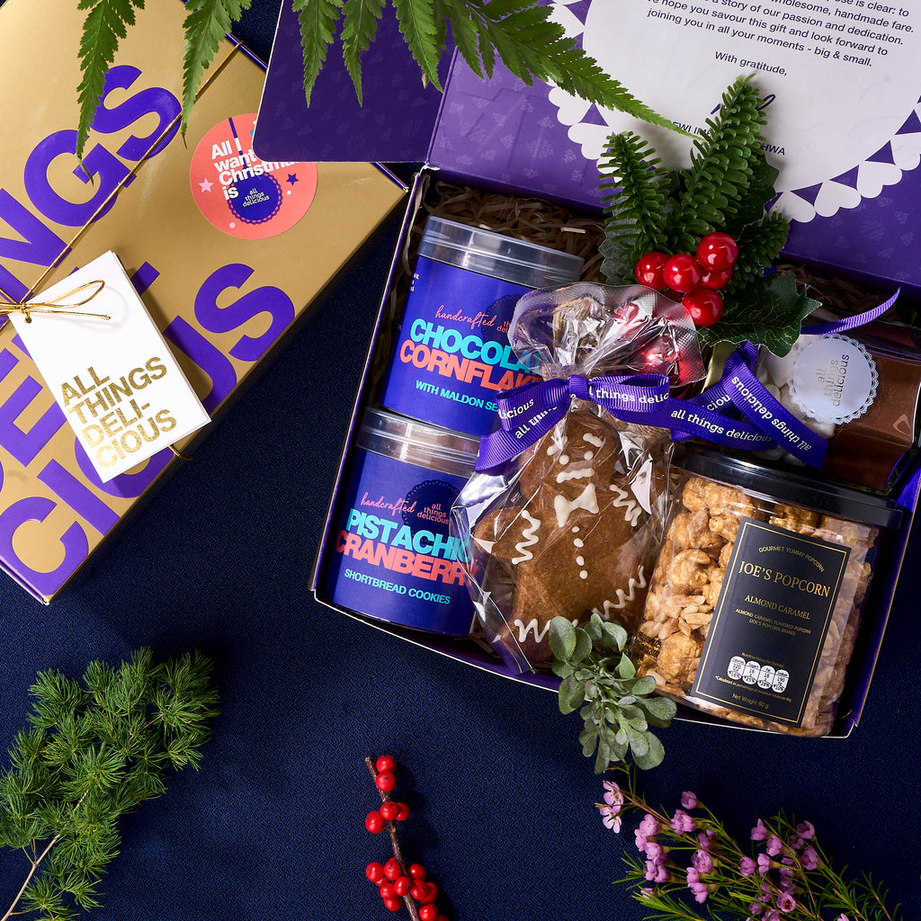 Open Christmas gift box holding cookie jars, popcorn and a ribboned gingerbread man